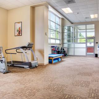 A spacious gym area with a treadmill and large windows letting in natural light.