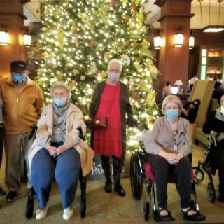 A group of people posing in front of a large, decorated Christmas tree, all wearing masks.