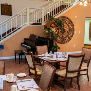 A cozy dining area with elegant table settings, a piano, and a decorative staircase in the background.