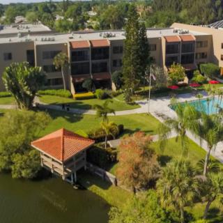 Aerial view of an apartment complex featuring a lake, dock, and swimming pool surrounded by lush greenery.
