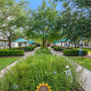 A beautifully landscaped garden with pathways, lush greenery, and outdoor seating areas under umbrellas.