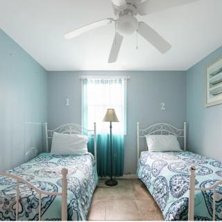 A cozy bedroom with twin beds, blue walls, and a ceiling fan.