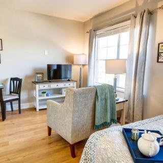 A cozy living room space featuring an armchair, a television on a console table, and a large window with curtains.