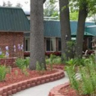 A brick building surrounded by trees and a landscaped garden with a pathway.