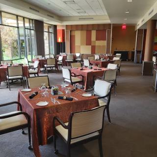 A spacious and elegantly arranged dining room with tables set for guests, featuring large windows that offer a view to the outdoors.