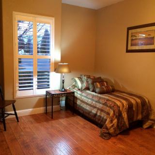 A cozy bedroom with a single bed, nightstand, and lamp, featuring warm lighting and a window with shutters.