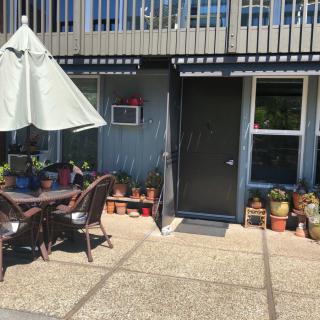 An inviting outdoor patio area with a sunshade, seating, and various potted plants.