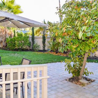 A peaceful backyard featuring a patio with furniture, an umbrella, and lush greenery.