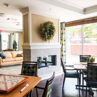 A modern lounge area featuring a central fireplace, tables with games, and comfortable seating bathed in natural light.