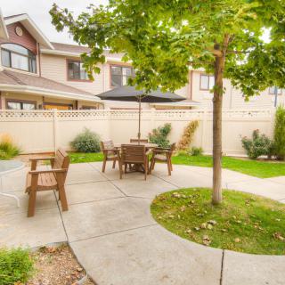 A cozy backyard patio with outdoor seating and a black umbrella, surrounded by greenery.
