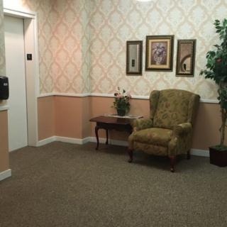 A quiet waiting area with an elevator, featuring a comfortable chair, side table, and decorative elements.