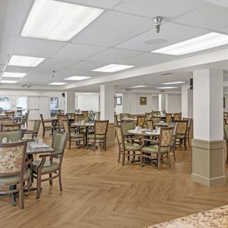 An empty dining room with neatly arranged tables and chairs, featuring a wooden floor and overhead lighting.