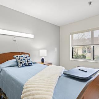 A serene and well-lit bedroom featuring a neatly made bed with blue bedding, decorative pillows, and a bedside table.