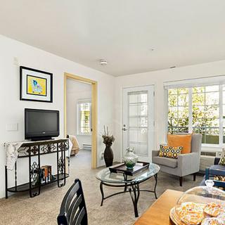A cozy living room with modern furniture, featuring a TV and large windows that let in natural light.
