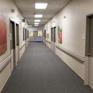 A view down a well-lit corridor featuring several doors and artwork on the walls.