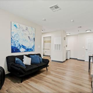 A modern living room with a black sofa, abstract artwork, and hardwood flooring.