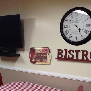 A cozy bistro-themed room with a large clock, TV, and red and white decor.