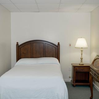 A simple bedroom with a single bed and a nightstand with a lamp.
