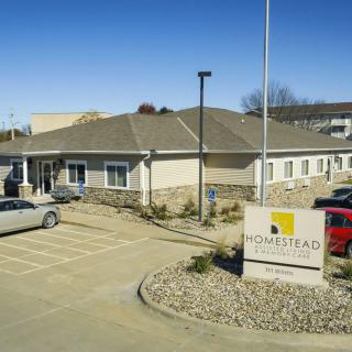 A view of a building with a parking lot and cars, featuring a sign in the foreground on a clear day.
