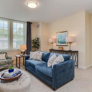 A cozy and well-decorated living room featuring a blue sofa, elegant lamps, and large windows.