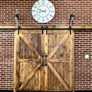 A rustic wooden barn door set against a brick wall, complemented by a vintage clock above.