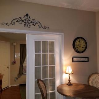 A cozy dining corner featuring a round table with chairs, decorative wall elements, a clock, and French doors.