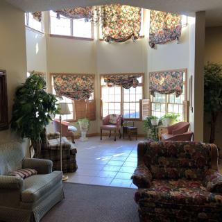 A cozy living room with ample natural light from large windows, featuring comfortable seating and lush indoor plants.