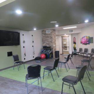 A modern meeting room with chairs arranged in a circle, featuring a TV and exercise equipment.
