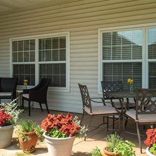A cozy patio area with chairs, a table, and potted plants in front of two large windows.