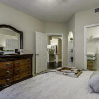 A cozy bedroom featuring a dresser with a mirror, an open door leading to another room, and decor in neutral tones.