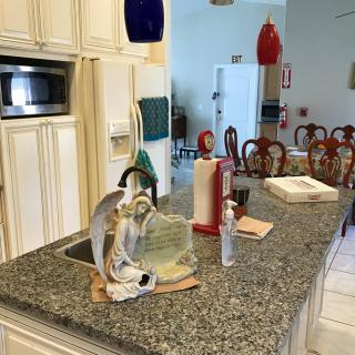 A kitchen with a granite countertop featuring a sink, dish soap, and dishes. A dining area is visible in the background.