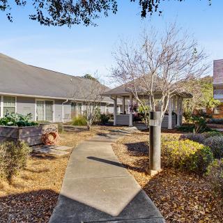 A scenic view of a landscaped pathway leading to a building surrounded by trees and bushes on a clear day.