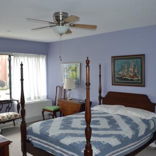 A cozy bedroom with a four-poster bed, ceiling fan, and decorative paintings.