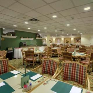 A spacious dining area with neatly arranged tables and chairs, featuring a green accent wall and carpeted flooring.
