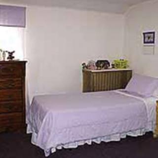 A simple bedroom with a single lavender-bedded bed and a dresser.