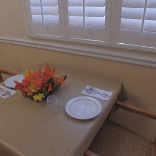 A dining table is set with a plate, napkins, and a floral centerpiece near a window.