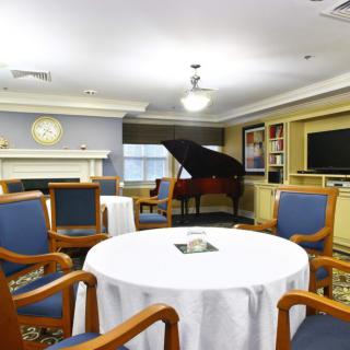 A cozy living room with a grand piano, surrounded by chairs and a round table with a white tablecloth.
