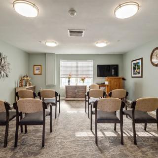 A small conference room with neatly arranged chairs facing a television, featuring soft lighting and tasteful decorations.