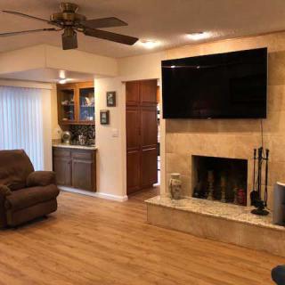 A cozy living room with a fireplace and television, featuring hardwood floors and a ceiling fan.