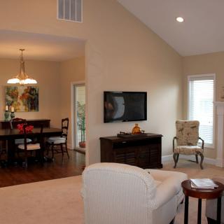A cozy living room with a connected dining area, featuring comfortable seating and a mounted TV.