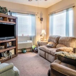 A cozy living room with a comfortable sofa, a television on a wooden bookshelf, and natural light streaming through the windows.