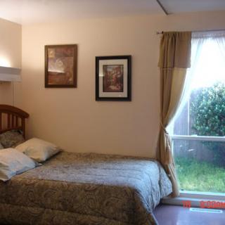 A cozy bedroom with a bed, framed pictures, and a large window with curtains.