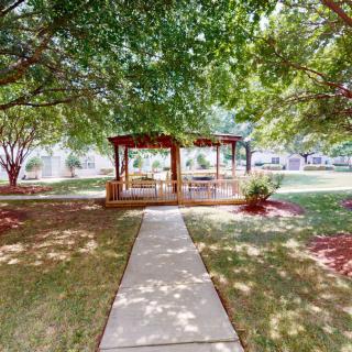 A peaceful garden with a pathway leading to a gazebo surrounded by lush trees.