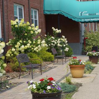 A charming garden pathway with blooming flowers and seating area under an awning.