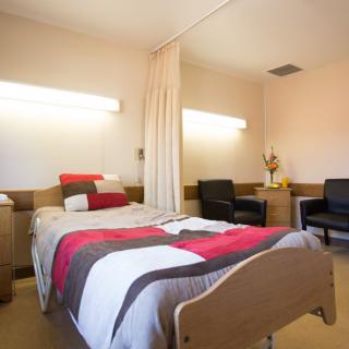 A well-furnished hospital room featuring a bed, chairs, and curtain for privacy.
