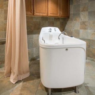 A modern walk-in bathtub with a curtain in a tiled bathroom.