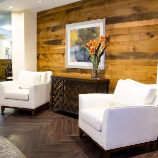 A modern living room features two white armchairs, a wooden accent wall, and a vase of orange flowers on a sideboard.