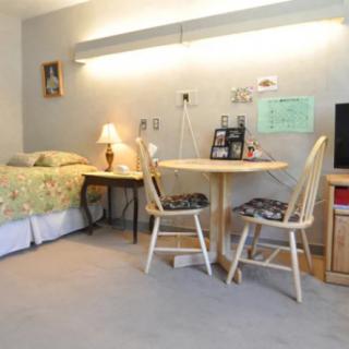 A cozy bedroom with a bed, round table, and chairs, lit by a table lamp.