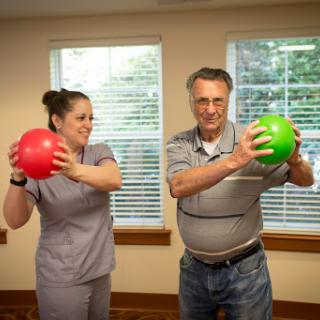 A healthcare professional and a senior participant engage in a fun exercise session using colored balls for rehabilitation.