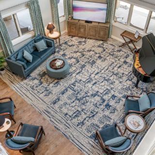 A spacious living room with blue furniture and a patterned rug, featuring a TV and multiple seating options.